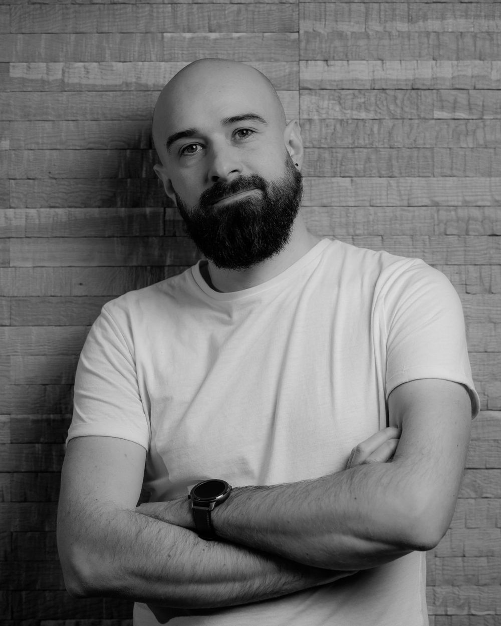 Csorvasi Csongor, black-and-white portrait, arms crossed in front of a wooden wall